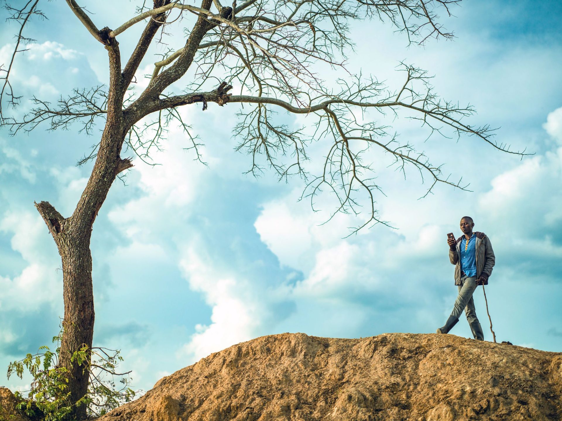 Man standing on a hill with a shovel, under a tree.