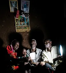 Family sitting together, illuminated by a small lamp. Click to learn more about energy.