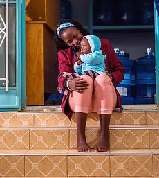 Woman sitting on steps holding a child in her lap. Click to learn more about health.