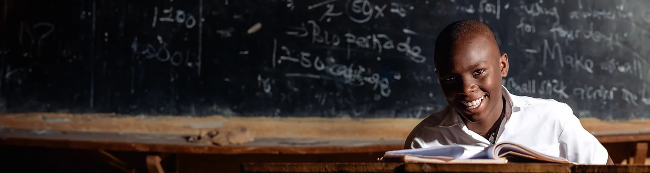 Smiling student reading a book in front of a chalkboard.