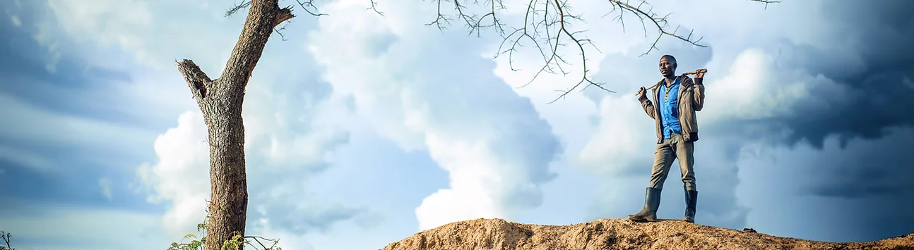 Man standing on a hill with a shovel over his shoulder.