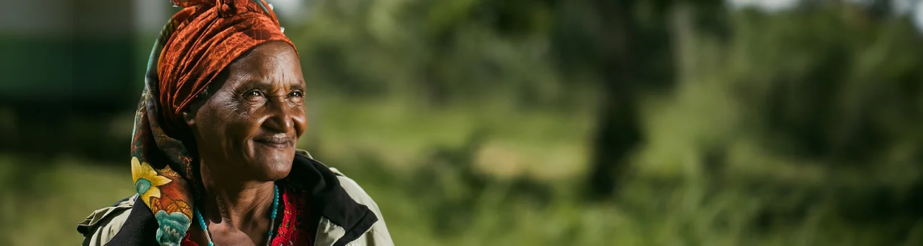 Smiling elderly woman wearing an orange headscarf in a green field.