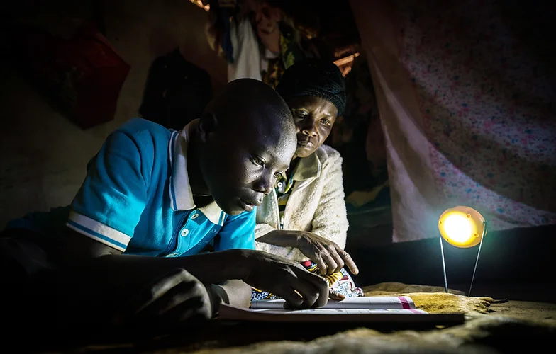 Boy studying with a woman under a small lamp.
