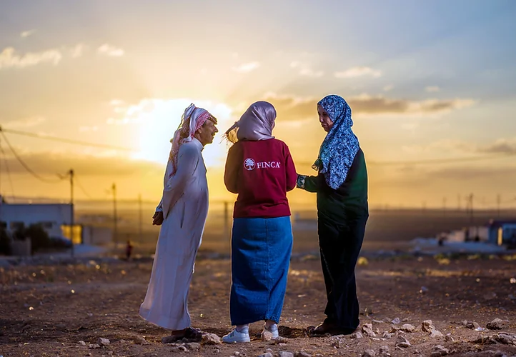 Three women talking at sunset in a rural area. One woman is wearing a FINCA shirt.